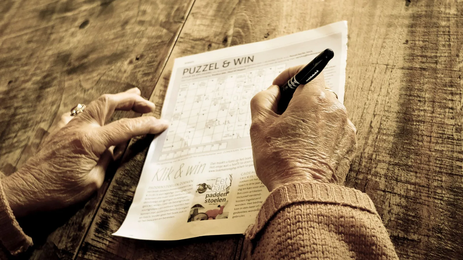 A senior adult working through a puzzle at a wooden table, a simple way to keep the mind engaged.