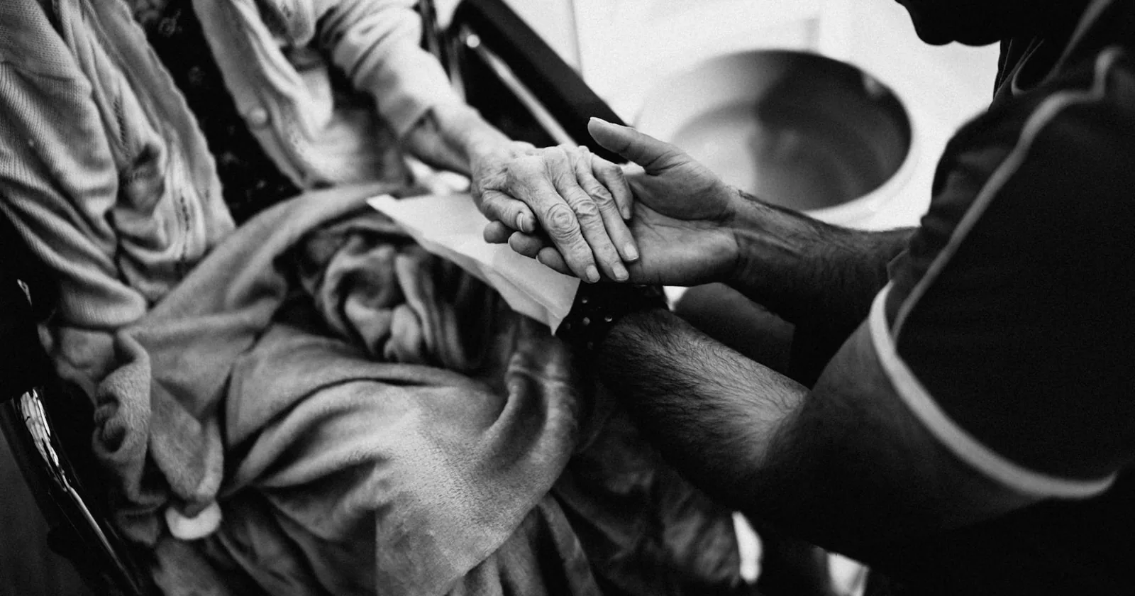 A caregiver gently holding the hands of an elderly woman seated in a wheelchair, a quiet moment of empathy and support.