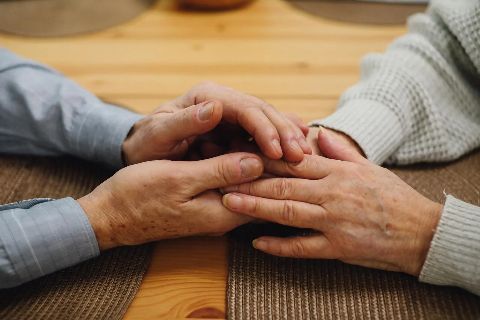 An elderly couple holding hands at a table, a quiet reminder that touch communicates care when words fail.