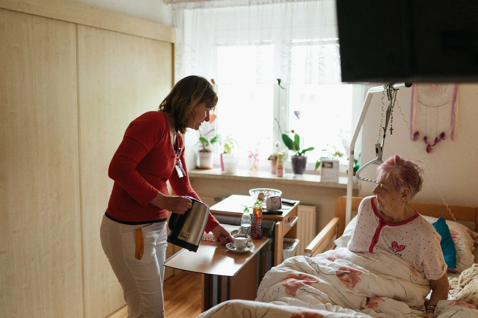 Caregiver serving tea to a senior woman in her bedroom