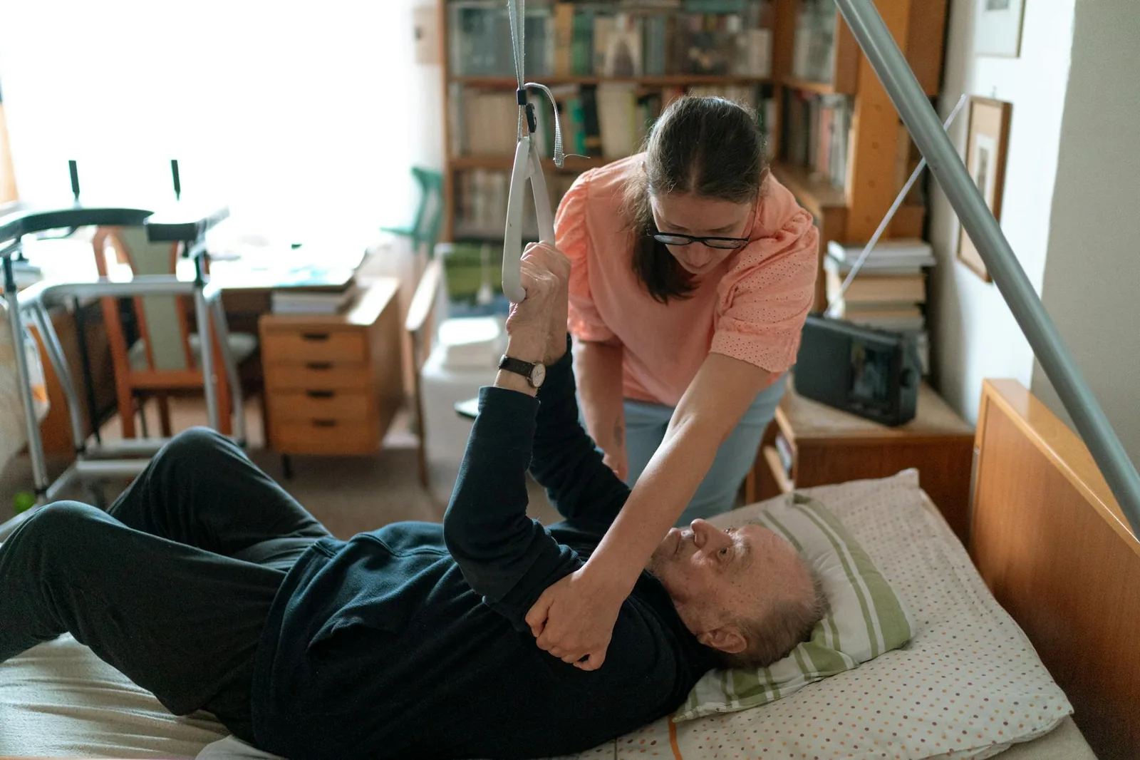 A home caregiver assisting an older man at home, a quiet moment of compassionate hands-on support.