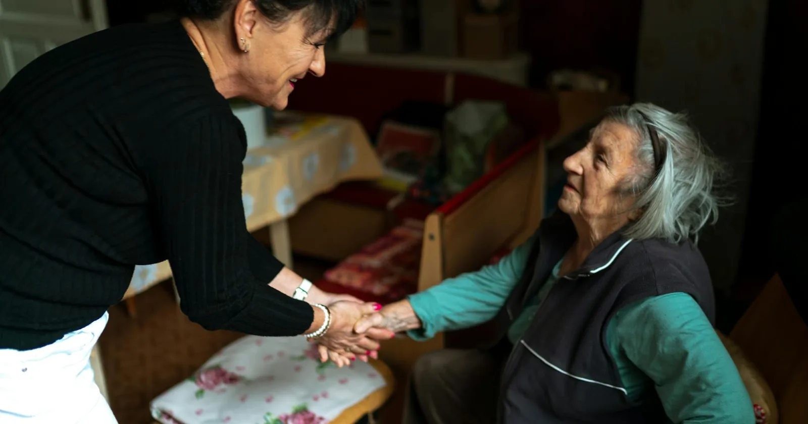 A home caregiver warmly greeting a senior woman in her living room.
