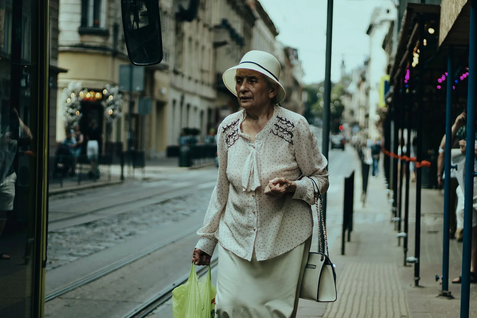 Senior woman in elegant attire walking down a city street carrying shopping bags.