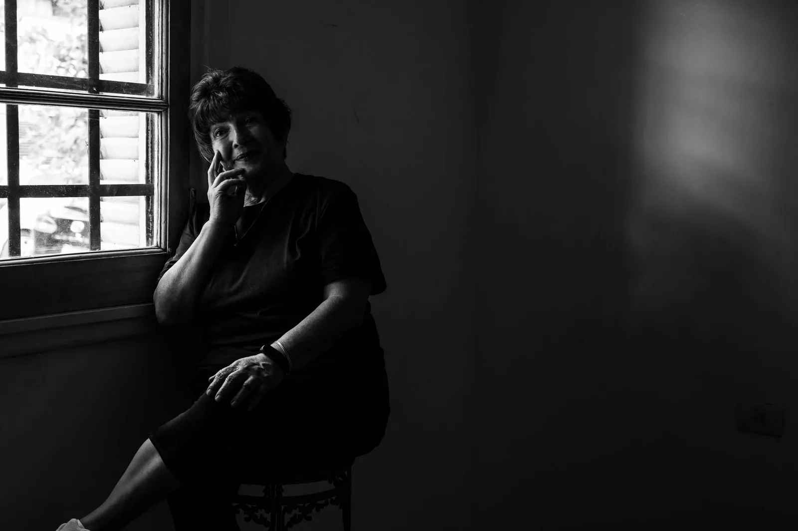 An older woman sitting beside a window in a bare room
