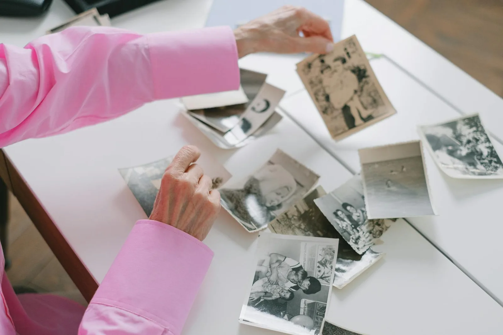 An elderly woman gently sorting through old black and white family photographs, a calming reminiscence activity.